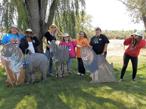 A group of adults standing behind cutouts of a tiger, elephant, zebra and a lion